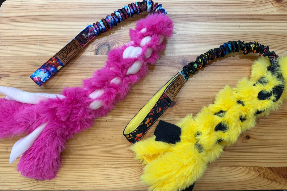 Two handmade braided fur agility tug toys with bungee handles, one pink and one yellow